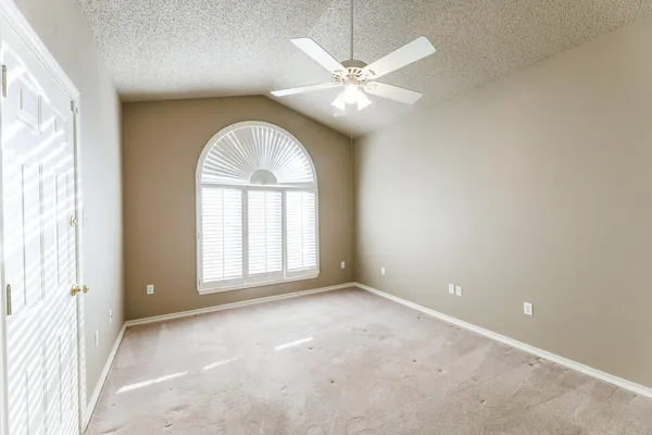 an empty room with a chandelier fan and kitchen view