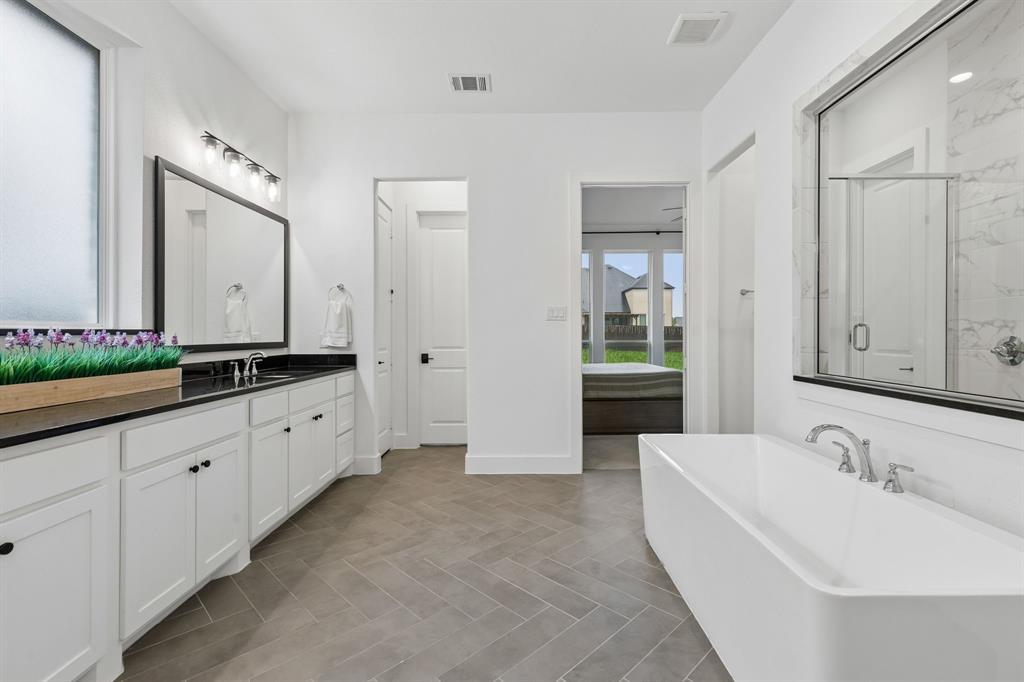 566 Broadleaf Way Haslet, TX 76052 - Photo 20 of 38 Spacious bathroom featuring a freestanding soaking tub, dual vanity with black countertops, rectangular mirrors, and a glass-enclosed shower with tile surround