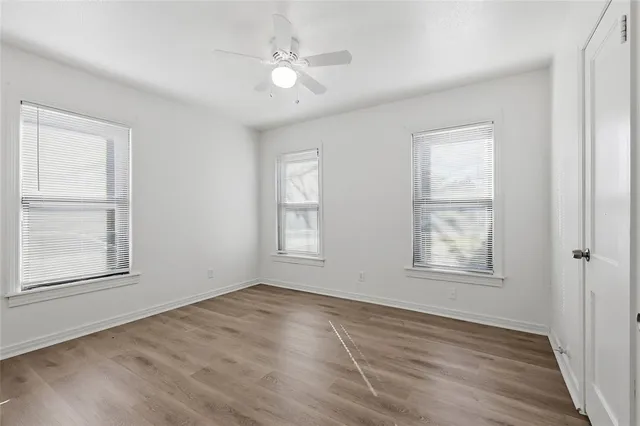 an empty room with wooden floor chandelier fan and windows