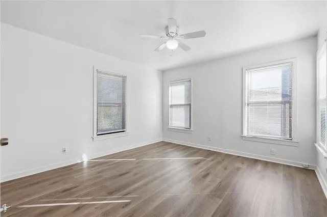 an empty room with wooden floor fan and windows