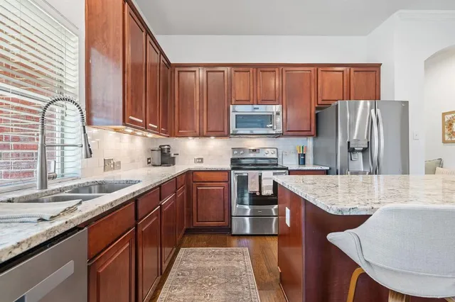 a kitchen with stainless steel appliances granite countertop a stove top oven a sink dishwasher and a refrigerator with wooden cabinets