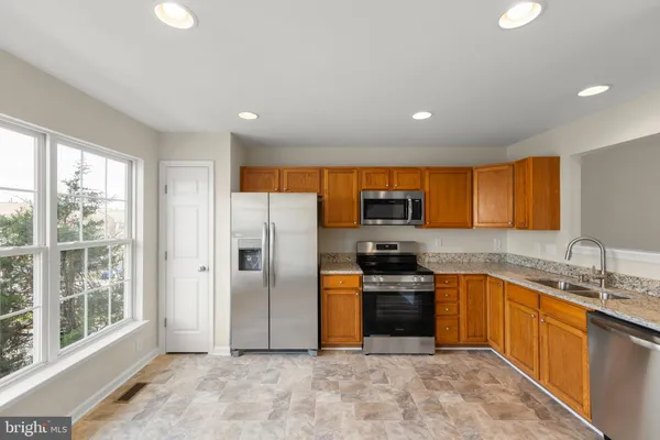 a kitchen with stainless steel appliances granite countertop a refrigerator a sink a stove top oven and a dishwasher next to a window