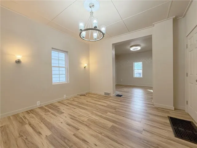 an empty room with wooden floor chandelier and windows