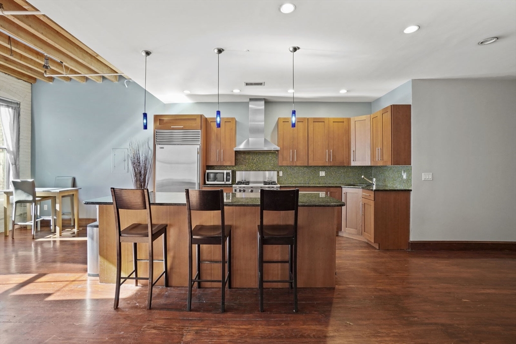 96 South Street, Unit 3 Boston, MA 02111 - Photo 11 of 17 a kitchen with stainless steel appliances kitchen island granite countertop a table chairs and a refrigerator