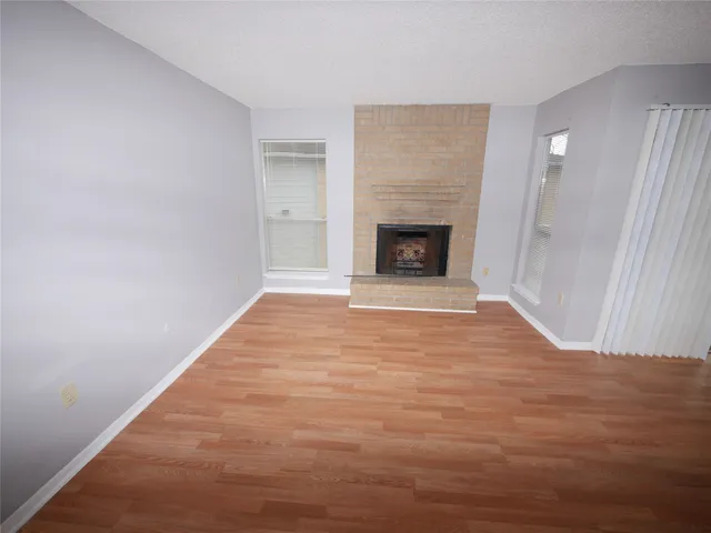 a view of an empty room with wooden floor fireplace and a window