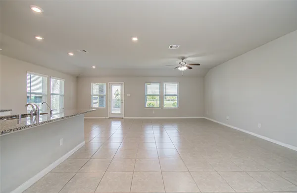 a view of an empty room with kitchen and window