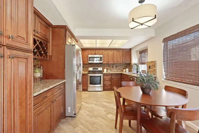 a kitchen with stainless steel appliances granite countertop a sink dishwasher a stove a refrigerator with a dining table and chairs