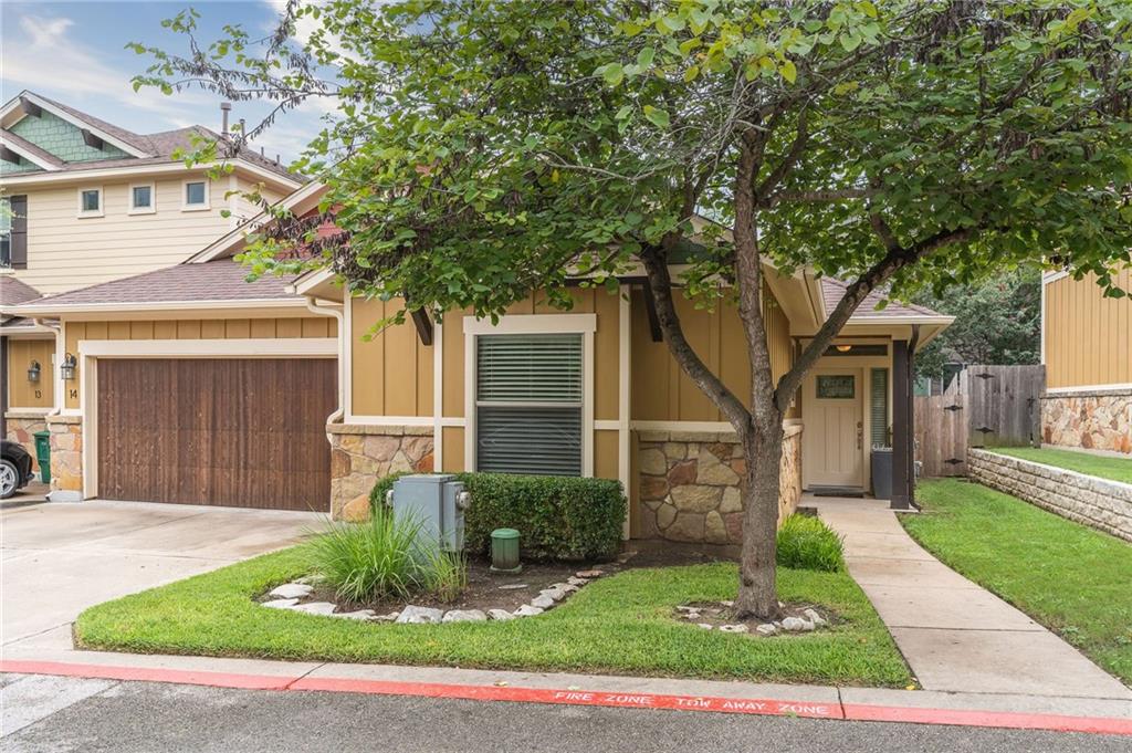 6708 Menchaca Road, Unit 14 Austin, TX 78745 - Photo 21 of 22 Single-story residence featuring a stone and siding exterior, a wood-finish garage door, a concrete walkway, a covered entry, and established landscaping