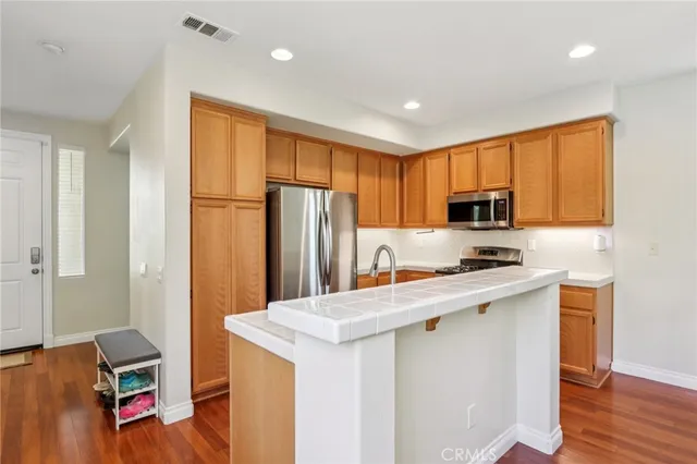 a kitchen with stainless steel appliances granite countertop a refrigerator a sink dishwasher a stove and white countertops with wooden floor