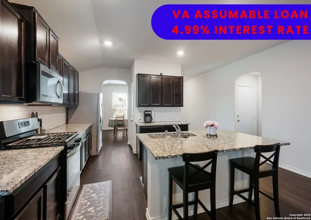 a kitchen with a granite countertop a stove a sink dishwasher a dining table and chairs with wooden floor