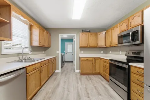 a kitchen with stainless steel appliances granite countertop wooden cabinets a stove top oven a sink and dishwasher with wooden floor