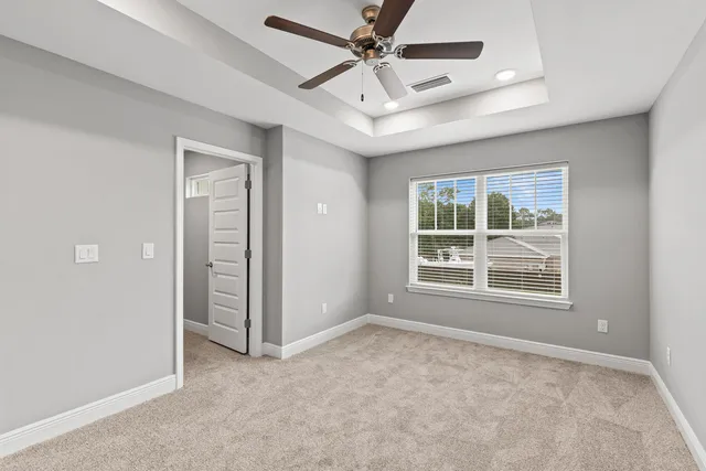 an empty room with chandelier fan and windows