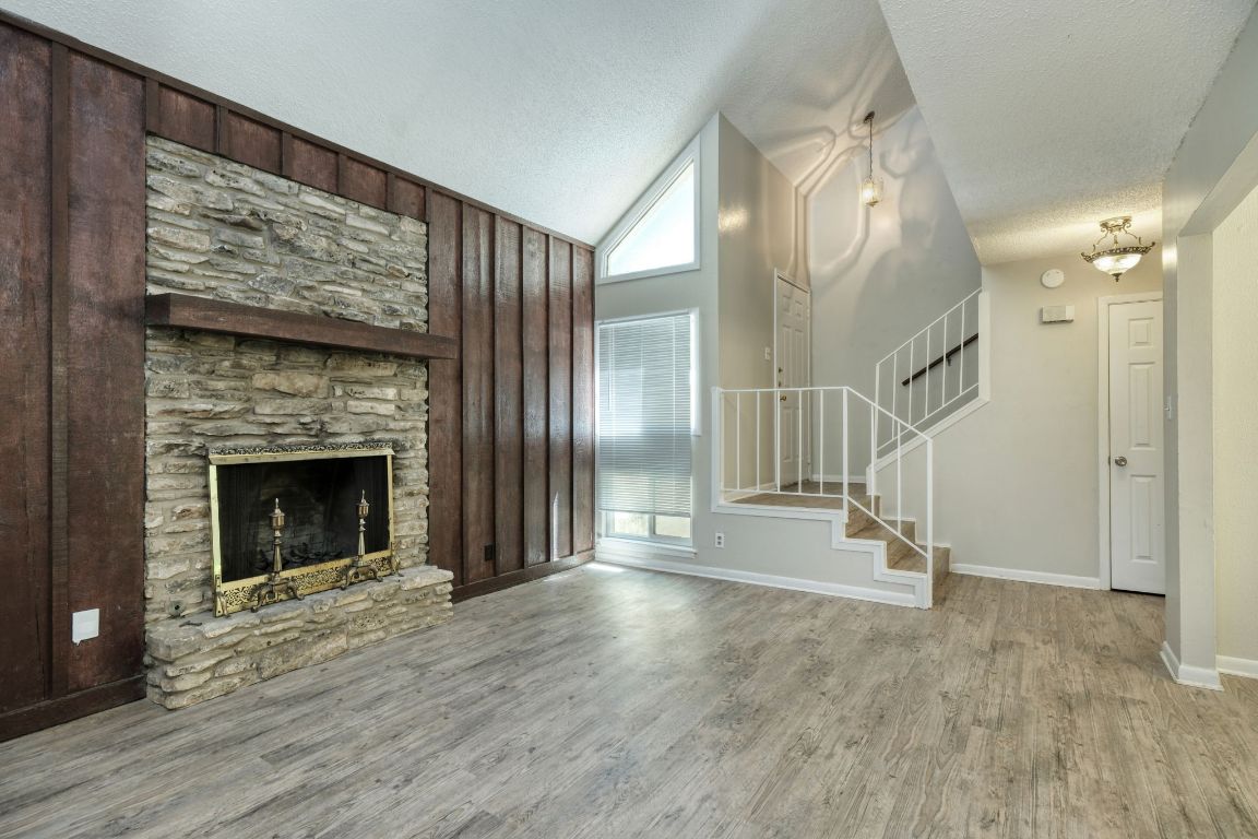 2711 St Edwards Circle, Unit 1 Austin, TX 78704 - Photo 3 of 14 Unfurnished living room featuring wood finished floors, stairway, a textured ceiling, high vaulted ceiling, and a fireplace
