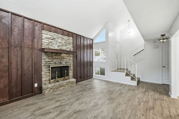 a view of an empty room with wooden floor fireplace and a window