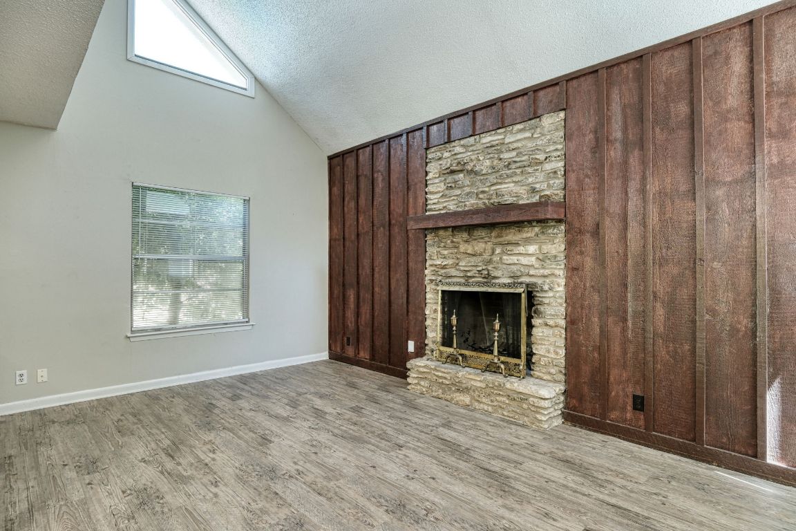 2711 St Edwards Circle, Unit 1 Austin, TX 78704 - Photo 4 of 14 Unfurnished living room featuring a textured ceiling, light wood-type flooring, a fireplace, high vaulted ceiling, and wood walls