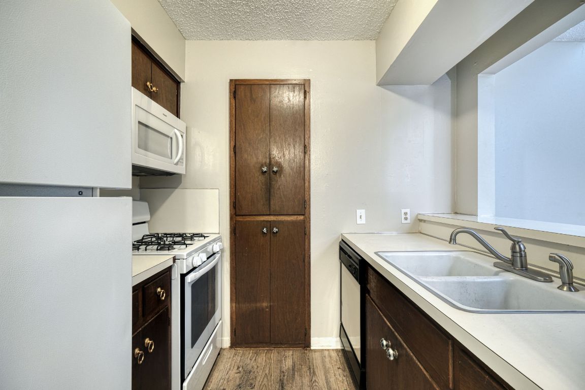 2711 St Edwards Circle, Unit 1 Austin, TX 78704 - Photo 6 of 14 Kitchen featuring dark brown cabinetry, white appliances, light countertops, dark wood-style floors, and a textured ceiling