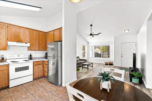 a kitchen with stainless steel appliances granite countertop a refrigerator a stove a sink a dining table and chairs with wooden floor