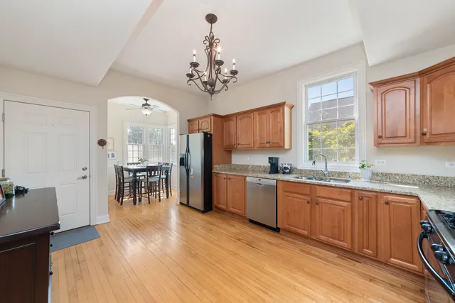 a open kitchen with stainless steel appliances granite countertop a refrigerator a stove a sink dishwasher a dining table and chairs with wooden floor