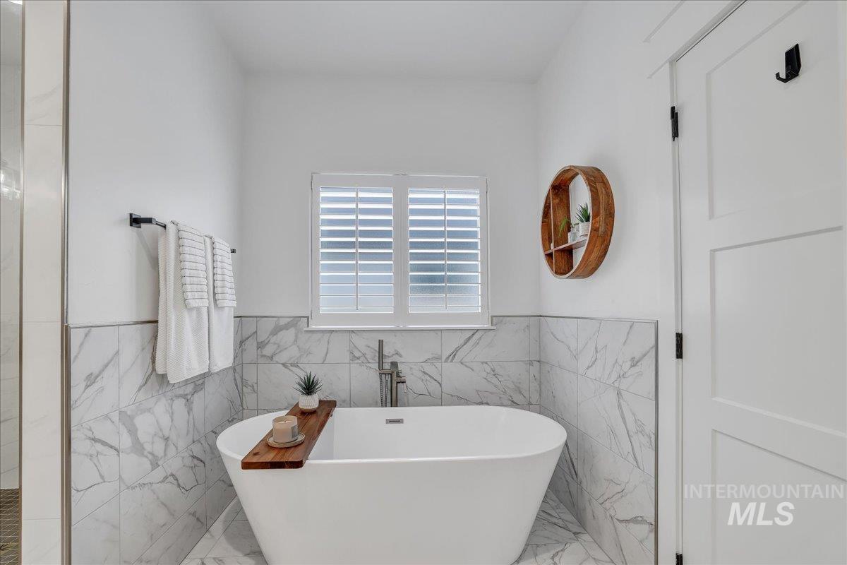2078 Red Rock Way Twin Falls, ID 83301 - Photo 31 of 49 Bathroom featuring marble look tile flooring, tile walls, a freestanding bath, and a wainscoted wall