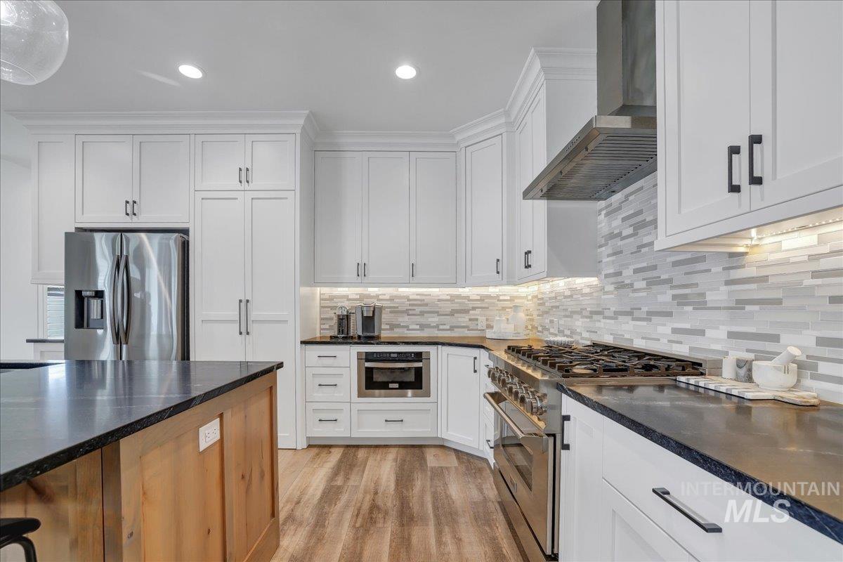 2078 Red Rock Way Twin Falls, ID 83301 - Photo 4 of 49 Kitchen featuring wall chimney range hood, appliances with stainless steel finishes, white cabinets, light wood-style flooring, and recessed lighting