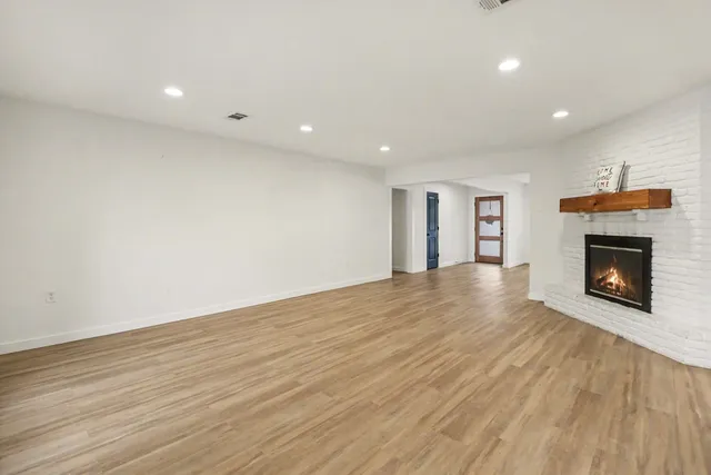 a view of an empty room with wooden floor fireplace and a window