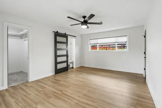 a view of an empty room with wooden floor and a ceiling fan