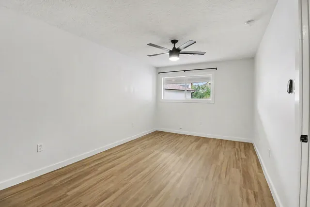 an empty room with wooden floor chandelier fan and windows