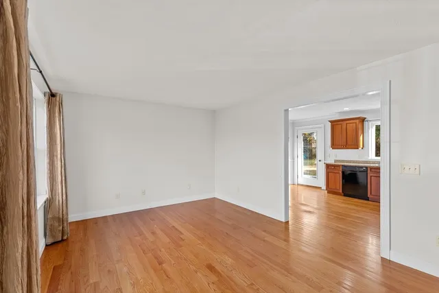 an empty room with wooden floor kitchen view and a window