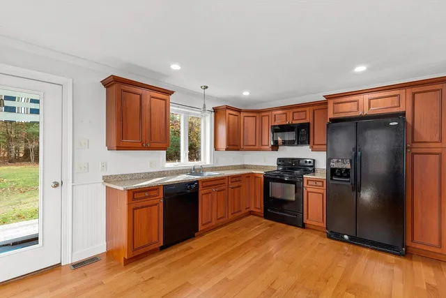 a kitchen with stainless steel appliances granite countertop a stove top oven a refrigerator and a sink with wooden floor