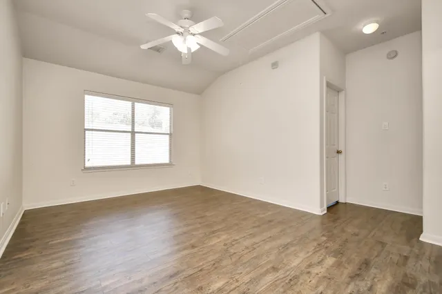 an empty room with wooden floor ceiling fan and windows