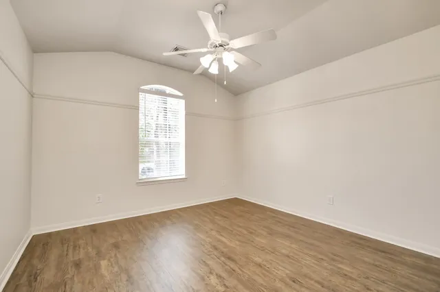an empty room with wooden floor chandelier fan and windows