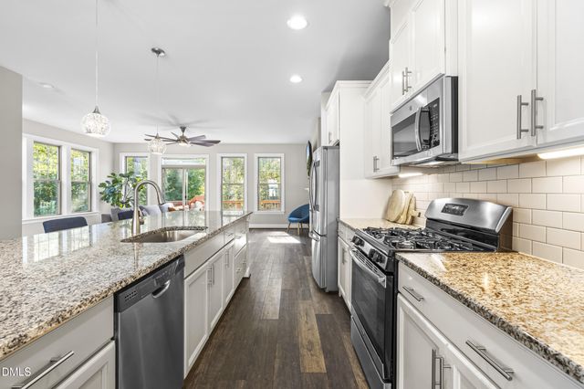 a kitchen with stainless steel appliances kitchen island granite countertop a dining table chairs and a refrigerator
