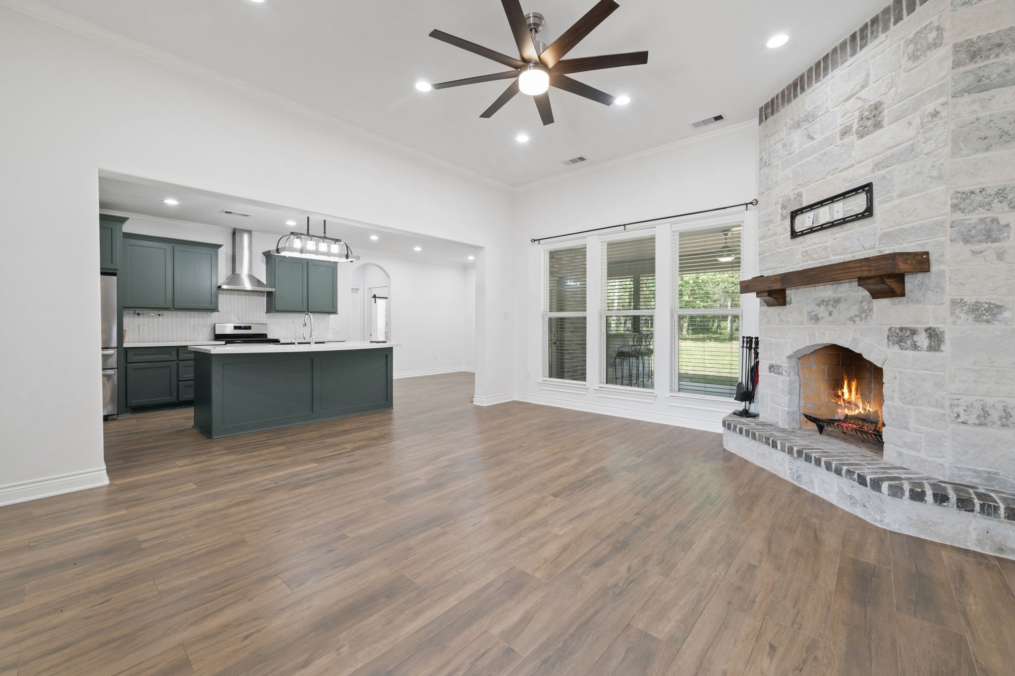 7815 Timber Switch Road Cleveland, TX 77328 - Photo 16 of 39 Spacious open-concept living area featuring a cozy stone fireplace, elegant hardwood floors, and a modern kitchen with stylish cabinetry and stainless steel appliances.