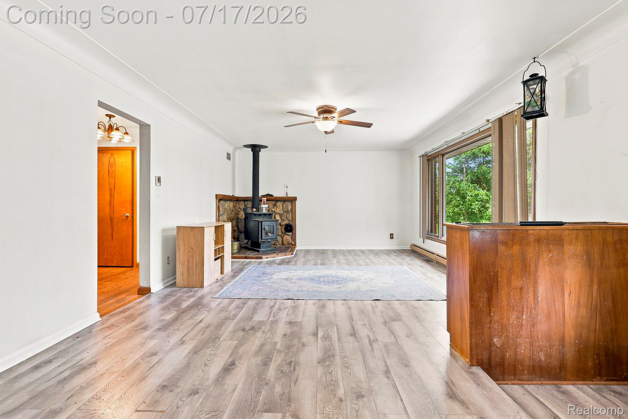 9805 Dolan Road Columbus, MI 48063 - Photo 2 of 39 Spacious room featuring wood-finish flooring, a stone hearth with a wood-burning stove, a ceiling fan, and a large window