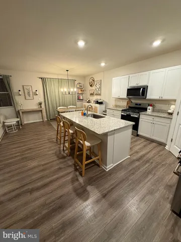 a living room with stainless steel appliances furniture wooden floor and a kitchen view