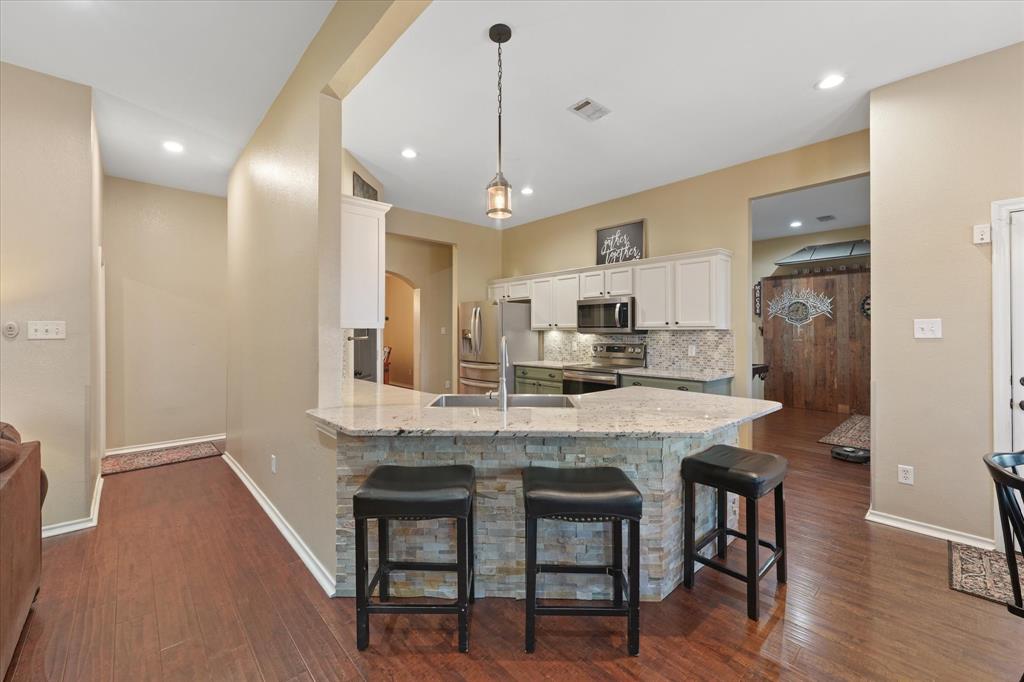 112 Springfield Lane Red Oak, TX 75165 - Photo 11 of 40 Kitchen featuring a peninsula with stone veneer base and light-toned, granite countertop, stainless steel appliances, white upper cabinetry, and a decorative mosaic tile backsplash