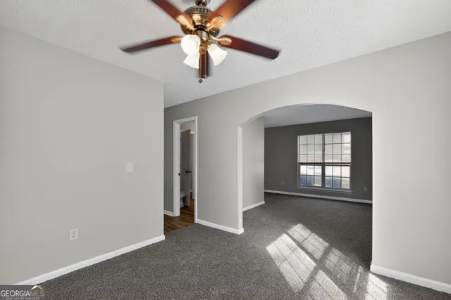 an empty room with chandelier fan and windows