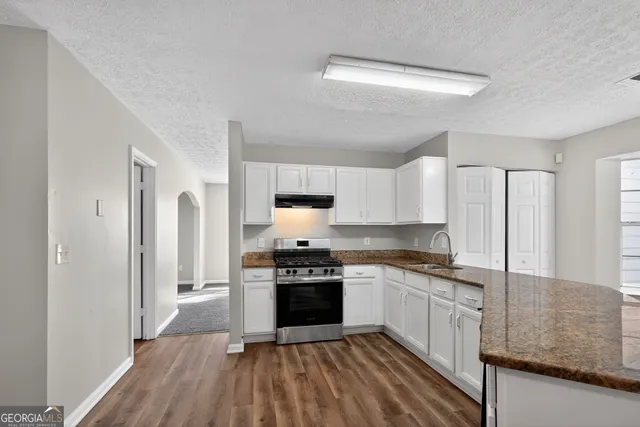 a kitchen with stainless steel appliances granite countertop a stove top oven a sink and white cabinets