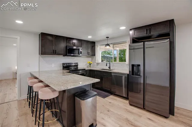 a kitchen with stainless steel appliances kitchen island granite countertop a dining table chairs and a refrigerator