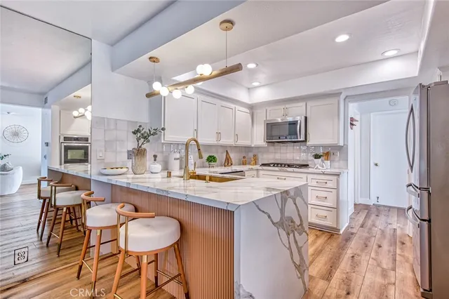 a kitchen with stainless steel appliances granite countertop a sink a stove a refrigerator and a dining table with wooden floor