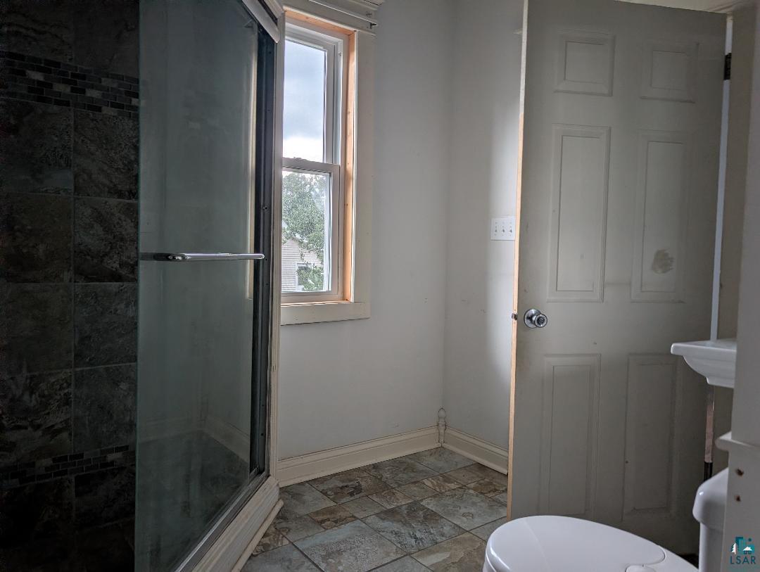 202 Thomas Street Mellen, WI 54546 - Photo 18 of 37 Tiled shower enclosure with a glass door, mosaic tile accent band, and a single-hung window with wood trim