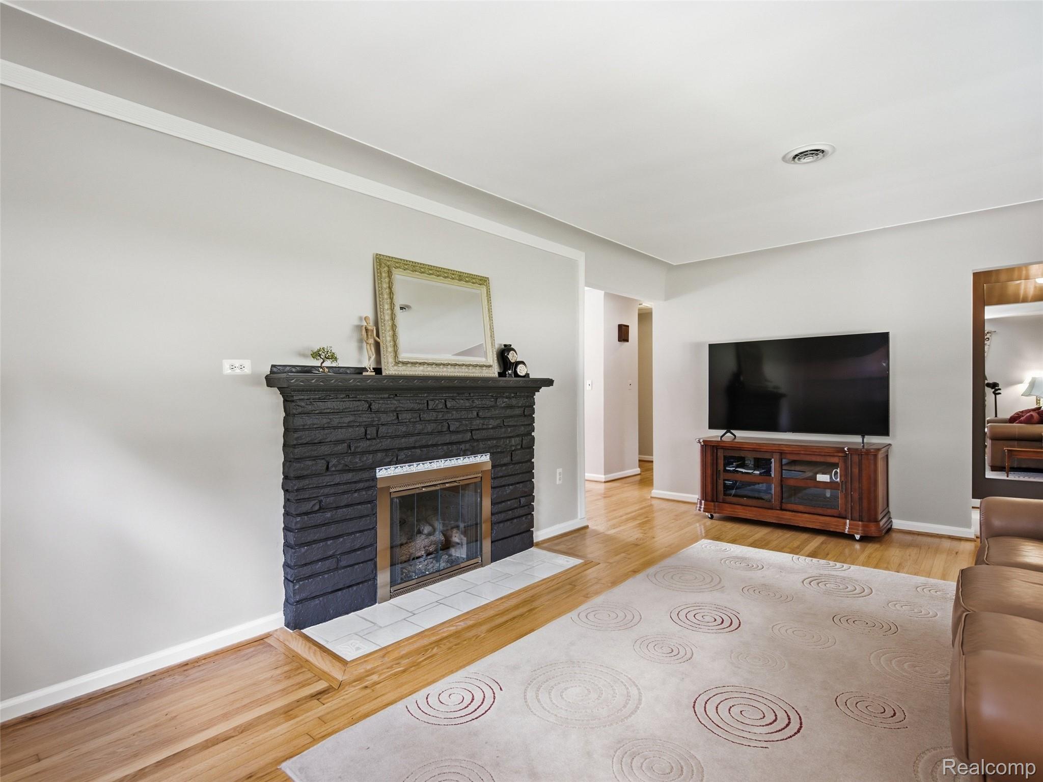 24 Nevada Avenue Rochester, MI 48309 - Photo 13 of 34 Living area featuring a black-stacked stone fireplace with a white tile hearth, wood-finish flooring, and light grey wall paint