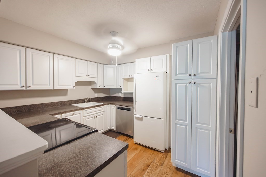 59 Brainerd Road, Unit 407 Boston, MA 02134 - Photo 9 of 22 a kitchen with a refrigerator a stove a sink and white cabinets with wooden floor