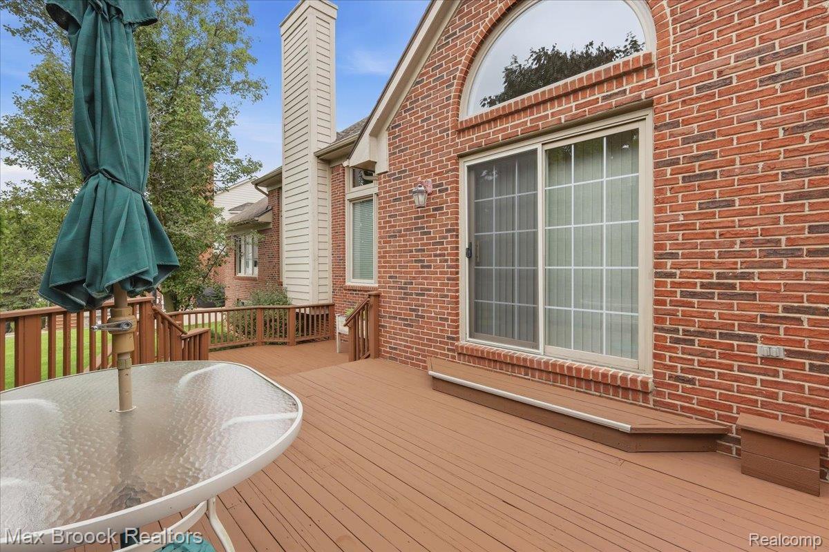 1731 Rico Road Commerce Township, MI 48382 - Photo 43 of 48 Expansive wood-finish deck with railing and steps, featuring a brick exterior, sliding glass door, and an arched transom window