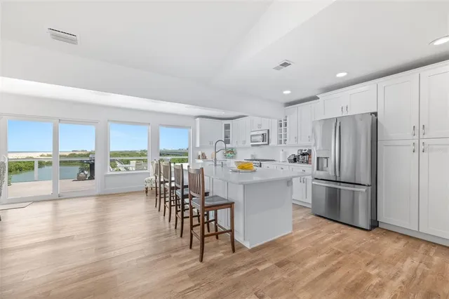 a kitchen with stainless steel appliances a refrigerator a stove a dining table and chairs with wooden floor