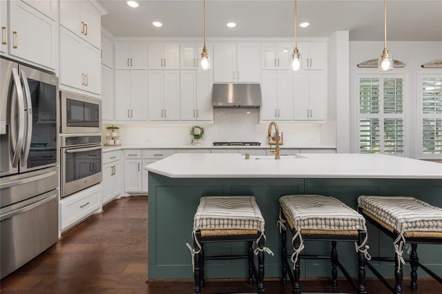 a kitchen with stainless steel appliances granite countertop a sink a stove a refrigerator and island with wooden floor