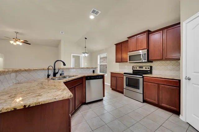 a large kitchen with granite countertop a stove top oven a sink dishwasher and wooden cabinets
