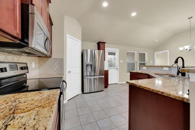 a kitchen with stainless steel appliances granite countertop a refrigerator a stove and a sink with wooden cabinets