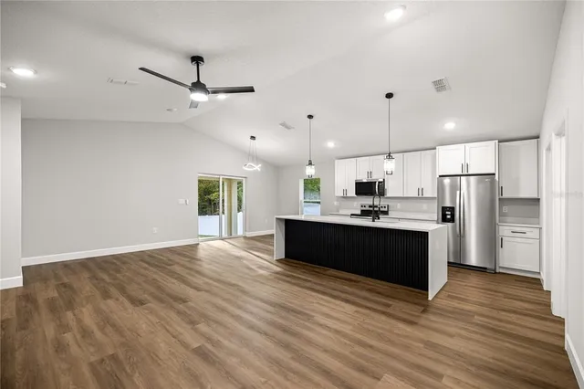 a large kitchen with kitchen island a island wooden floor stainless steel appliances and a window