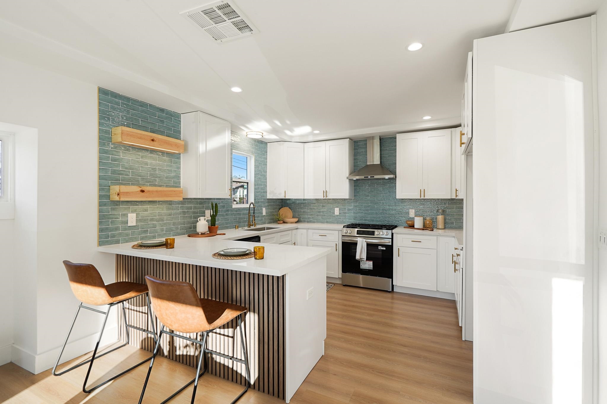 2151 Santa Rita Street Oakland, CA 94601 - Photo 7 of 46 Kitchen featuring stainless steel range with gas stovetop, decorative backsplash, wall chimney exhaust hood, a breakfast bar area, and light wood-type flooring